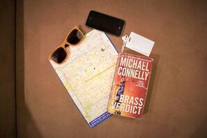 A book titled "The Brass Verdict" by Michael Connelly, a pair of sunglasses, a smartphone, and a map. - Studio'Z (Chiang Mai)