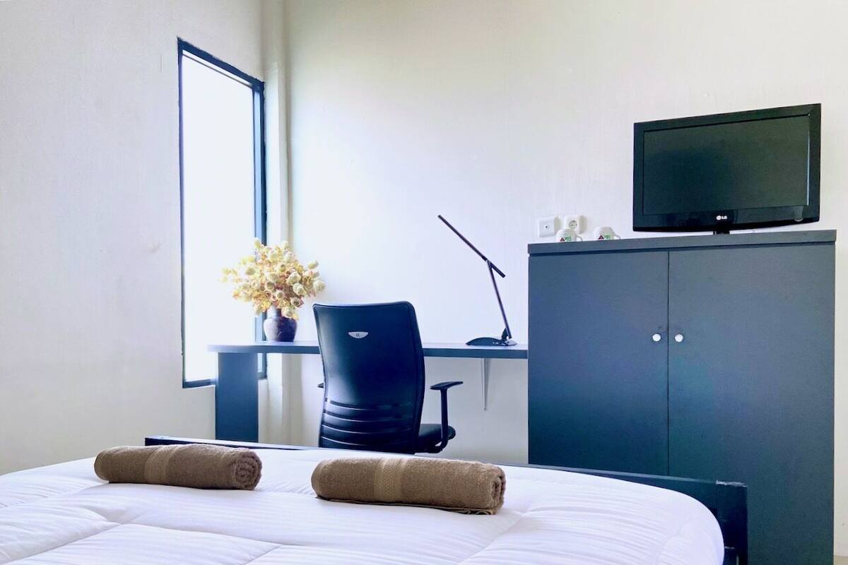 A hotel room with a large bed, a desk with a chair, a television on a cabinet, and a window with a view of the sky.
