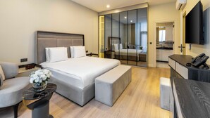 Ein modernes Hotelzimmer mit einem großen Bett, einer Sitzecke, einem kleinen Tisch mit Blumen, einem Fernseher und einem separaten Badezimmer.