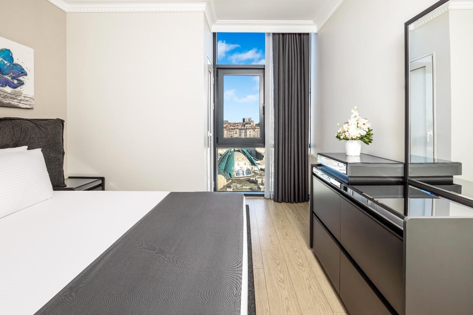 Ein modernes Hotelzimmer mit Bett, Schreibtisch, Spiegel und Blick auf die Stadt.