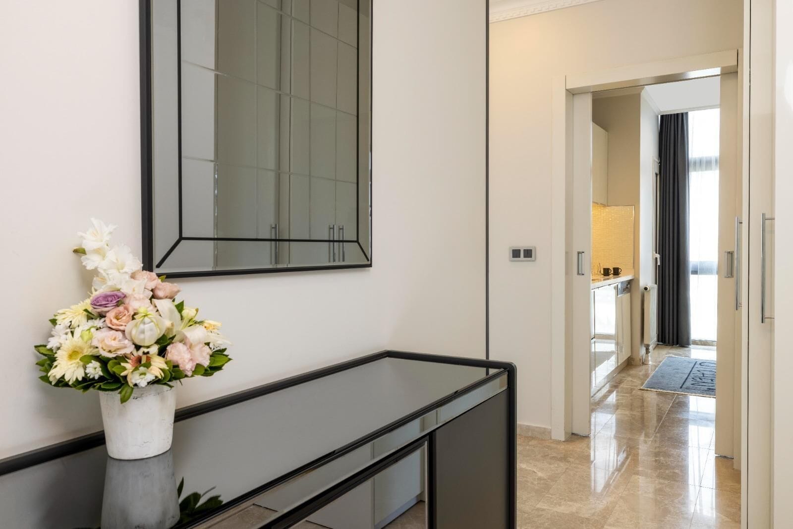 A modern hotel lobby with a long reception desk, a large mirror, and a vase of flowers.