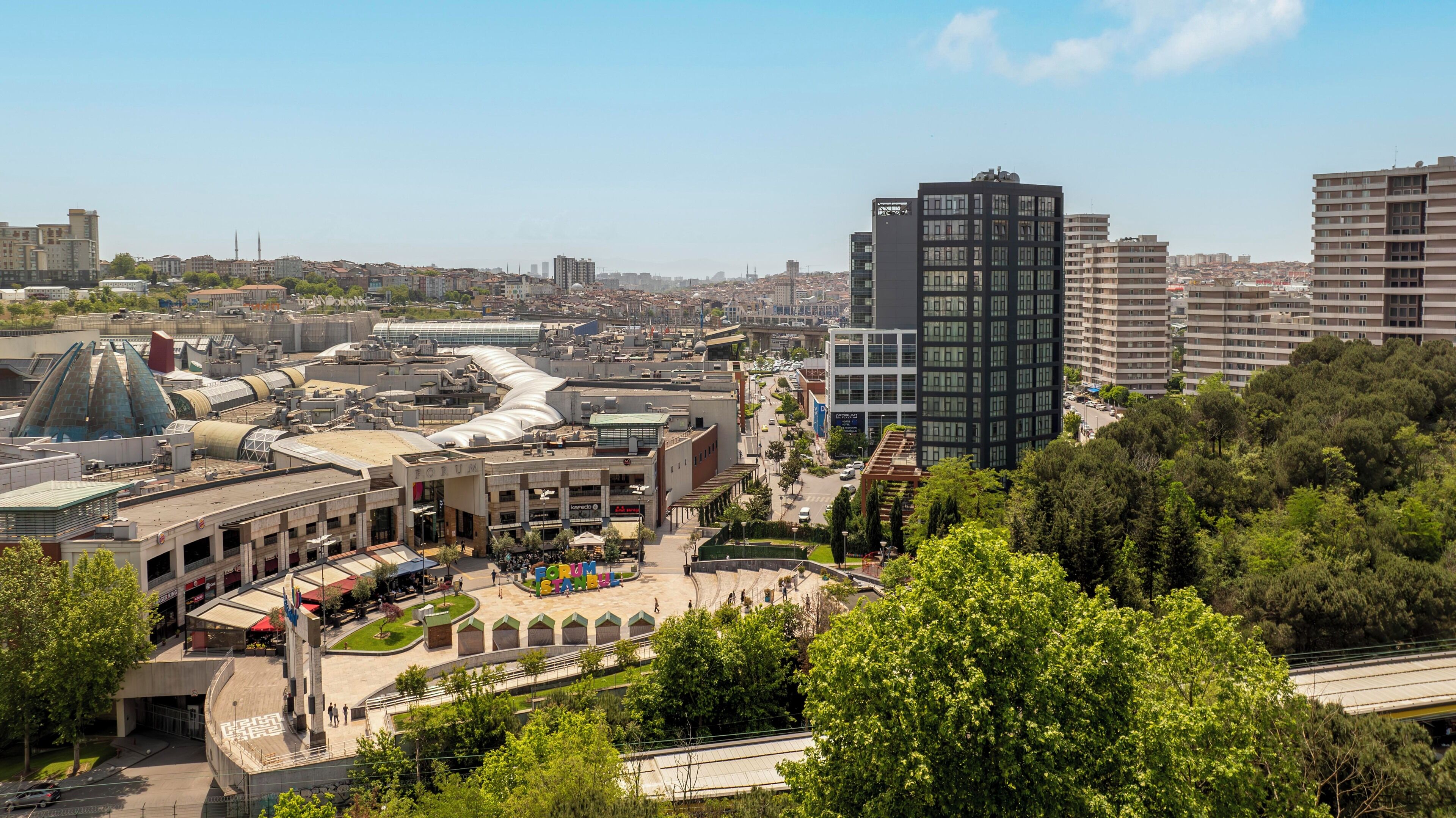 Un paysage urbain avec des bâtiments modernes, une vaste place publique agrémentée de bancs et une imposante structure en forme de dôme.