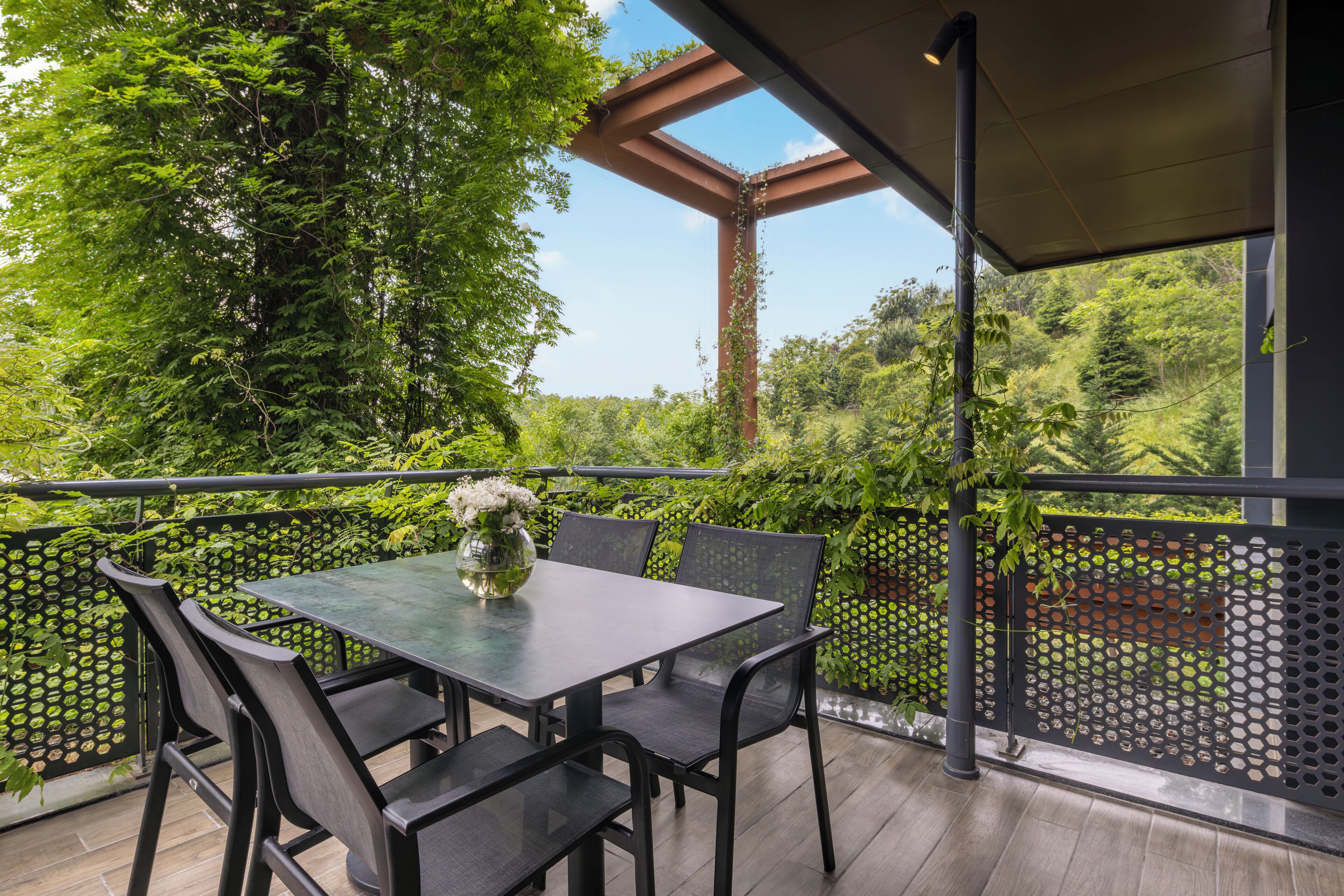 Un balcón con mesa y sillas, rodeado de vegetación y vistas al bosque.