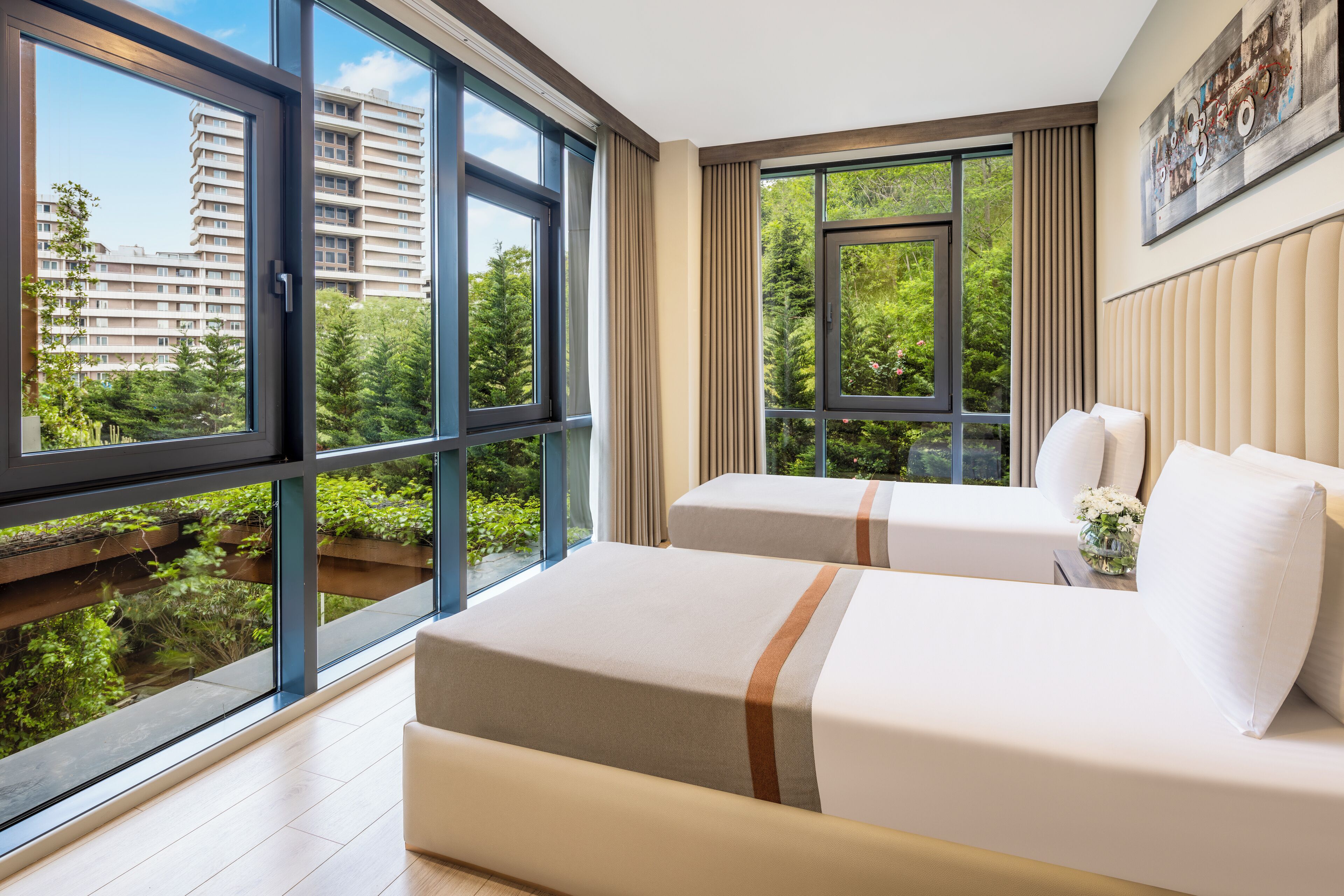A hotel room with two beds, large windows, and a view of a building and greenery.