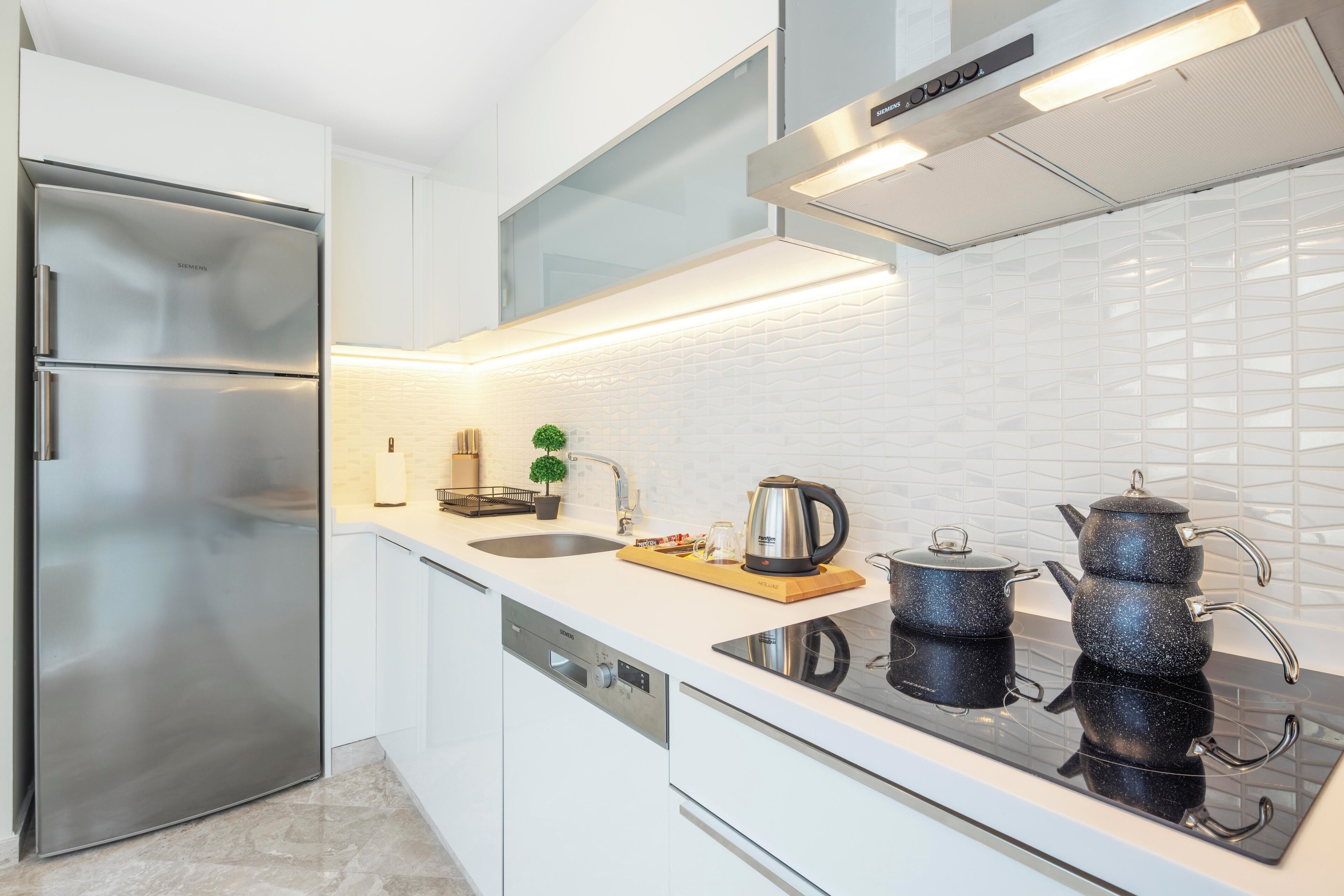 A modern kitchen with stainless steel appliances, a black induction cooktop, and white cabinetry.