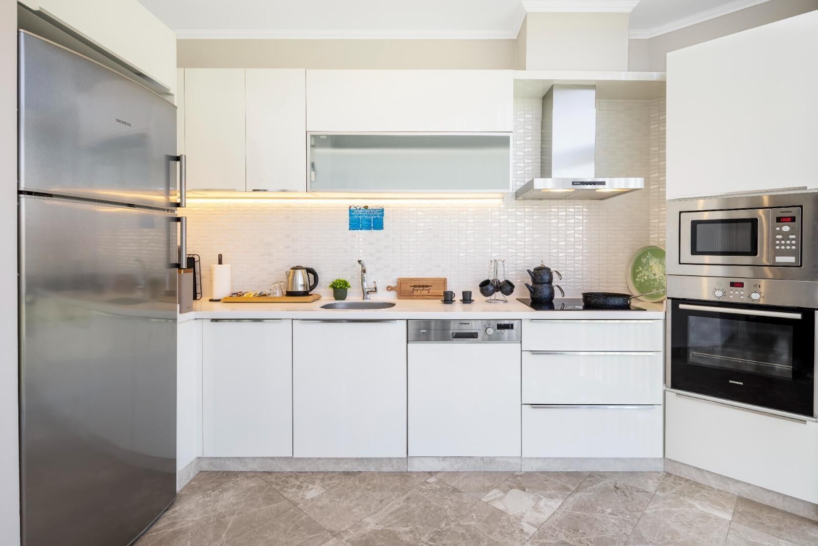 Een moderne keuken met roestvrijstalen apparatuur, witte kastjes en een betegelde achterwand.