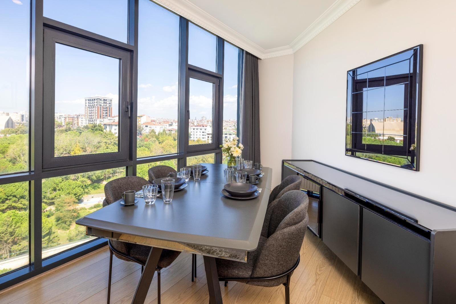 Een moderne eetruimte met een grote tafel voor vier personen, grote ramen met uitzicht op de stad en een ingebouwd aanrecht.