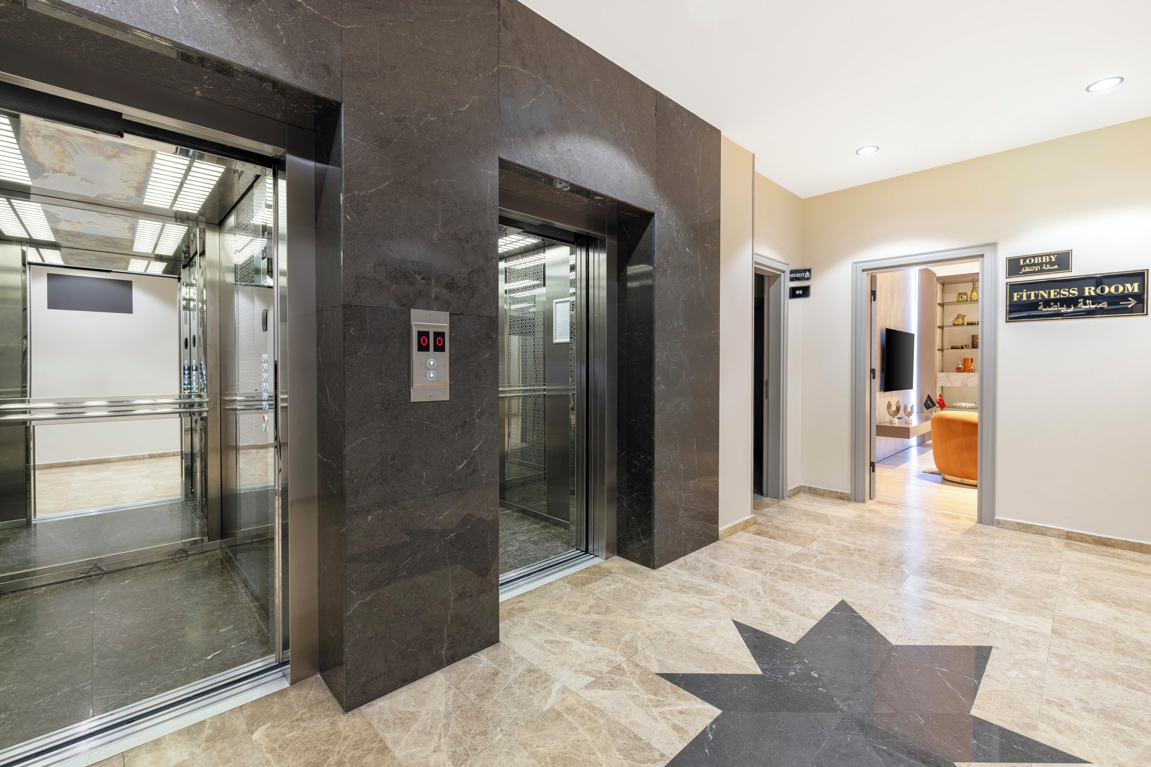 An elevator area with a star-shaped floor design, a fitness room sign, and a lobby sign.