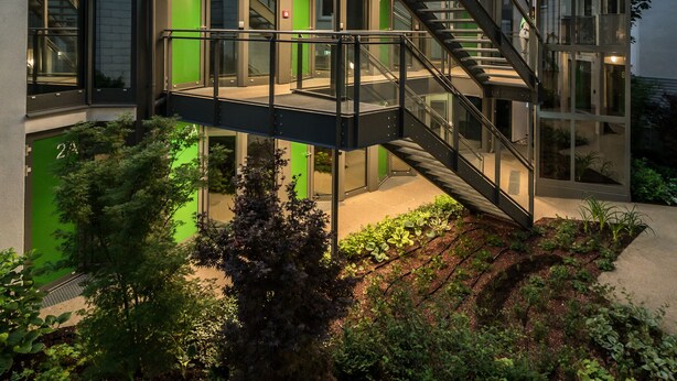 Een modern gebouw met een glazen trap, meerdere balkons en een goed verlichte ingang.