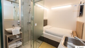 Een moderne badkamer met een douchecabine van glas, een wastafel en een bed.