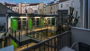 Een modern gebouw met meerdere verdiepingen, glazen balkonhekken en genummerde deuren die verschillende kamers of appartementen aangeven.