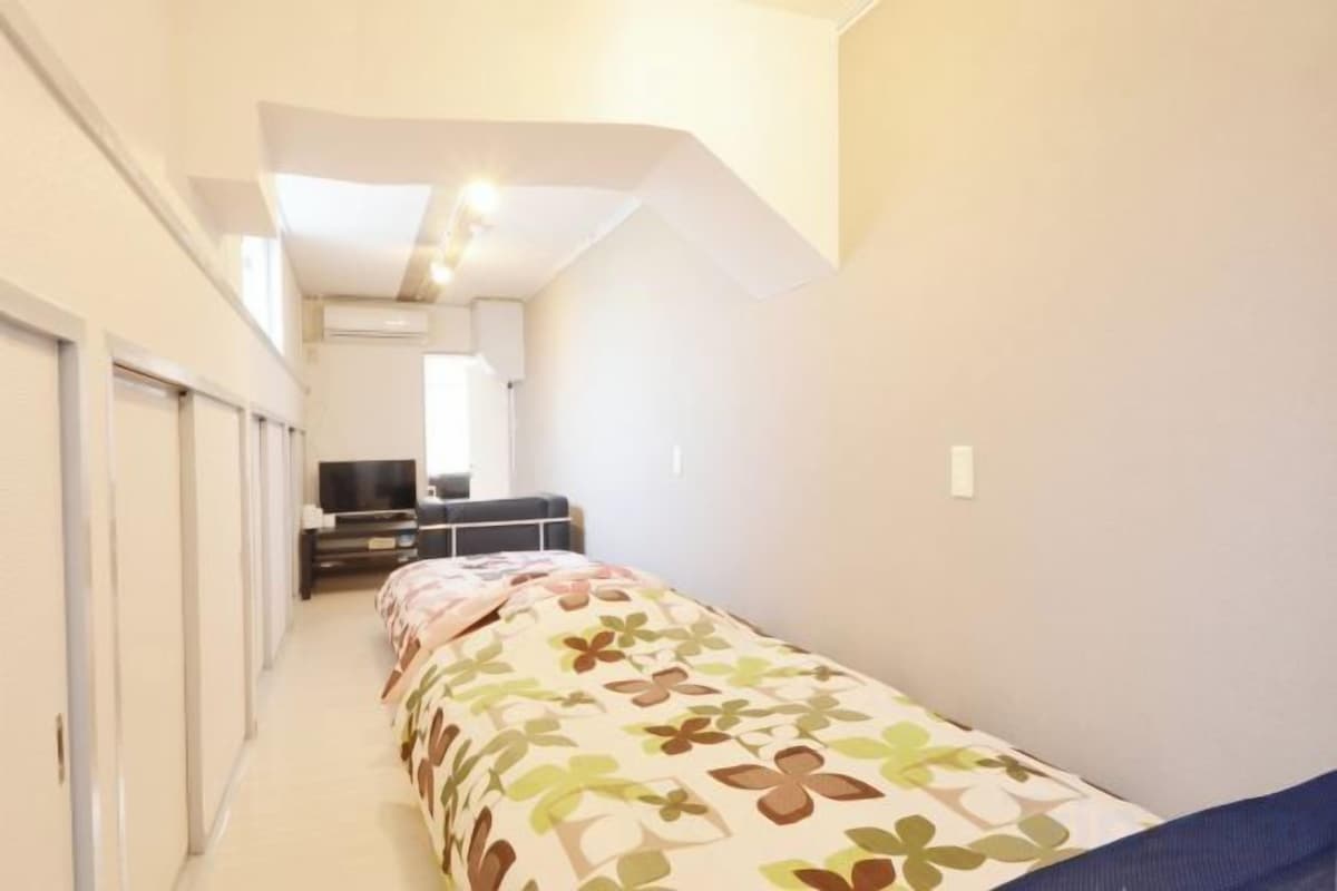 A narrow hallway leading to a bedroom with a bed, a dresser, and a television.