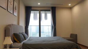 A hotel room with a large bed, a chair, a nightstand, and a window with curtains.