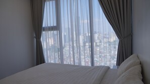 A bedroom with a large window, a bed, and curtains.