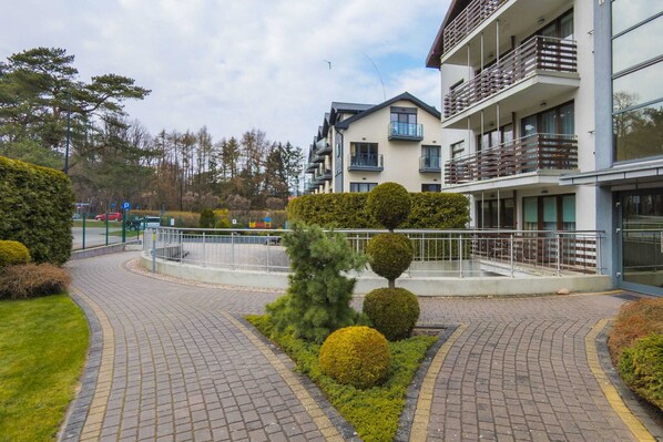 A modern building with a courtyard, a paved walkway, and neatly trimmed bushes.