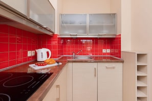 Une cuisine moderne avec des carreaux rouges, une plaque de cuisson à induction noire, une bouilloire blanche et un évier.