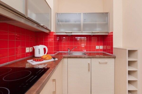 A modern kitchen with red tiles, a black induction cooktop, a white kettle, and a sink.