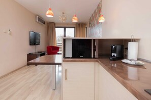 A modern living room with a wooden floor, a red chair, a flat-screen TV, a coffee machine, and a large window.