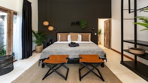 Quarto moderno com uma cama grande, duas poltronas, uma mesinha, um vaso de planta e uma estante com objetos decorativos.