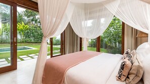 Quarto com cama grande, cortinas leves e vista para o jardim e piscina.