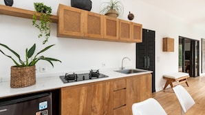 A modern kitchen with wooden cabinets, a built-in stove, and a sink. There is a potted plant on the counter and a dining area with a bench and chairs. - Elegant 2BR Villa W/ Pool, Bali Villa 2221 (Canggu)