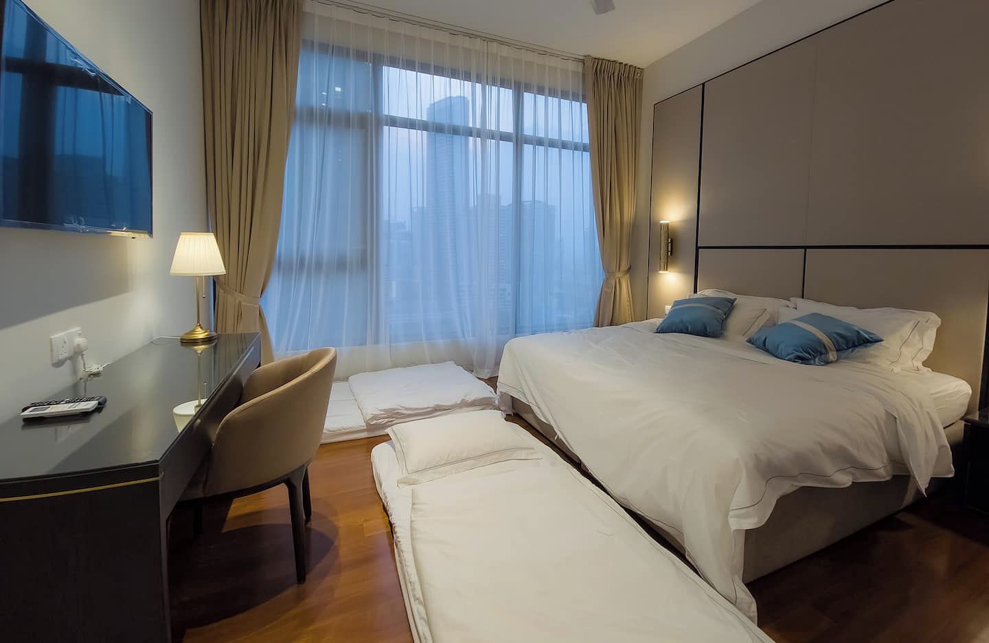 Een hotelkamer met een bed, bureau, stoel en een groot raam met gordijnen.