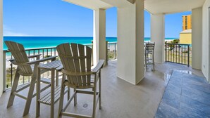 Un balcón con dos sillas Adirondack y una mesa, con vista a una playa y el océano.