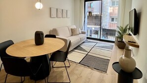 Ein modernes Wohnzimmer mit einem runden Holzesstisch, schwarzen Stühlen, einem weißen Sofa und einem großen Fenster mit Blick auf Gebäude.