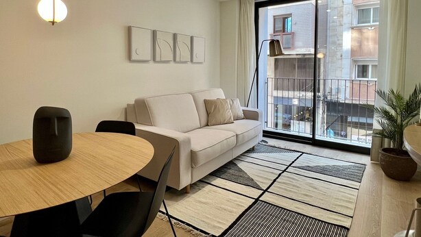 Ein modernes Wohnzimmer mit einer Couch, einem runden Tisch und einem großen Fenster mit Blick auf Gebäude.