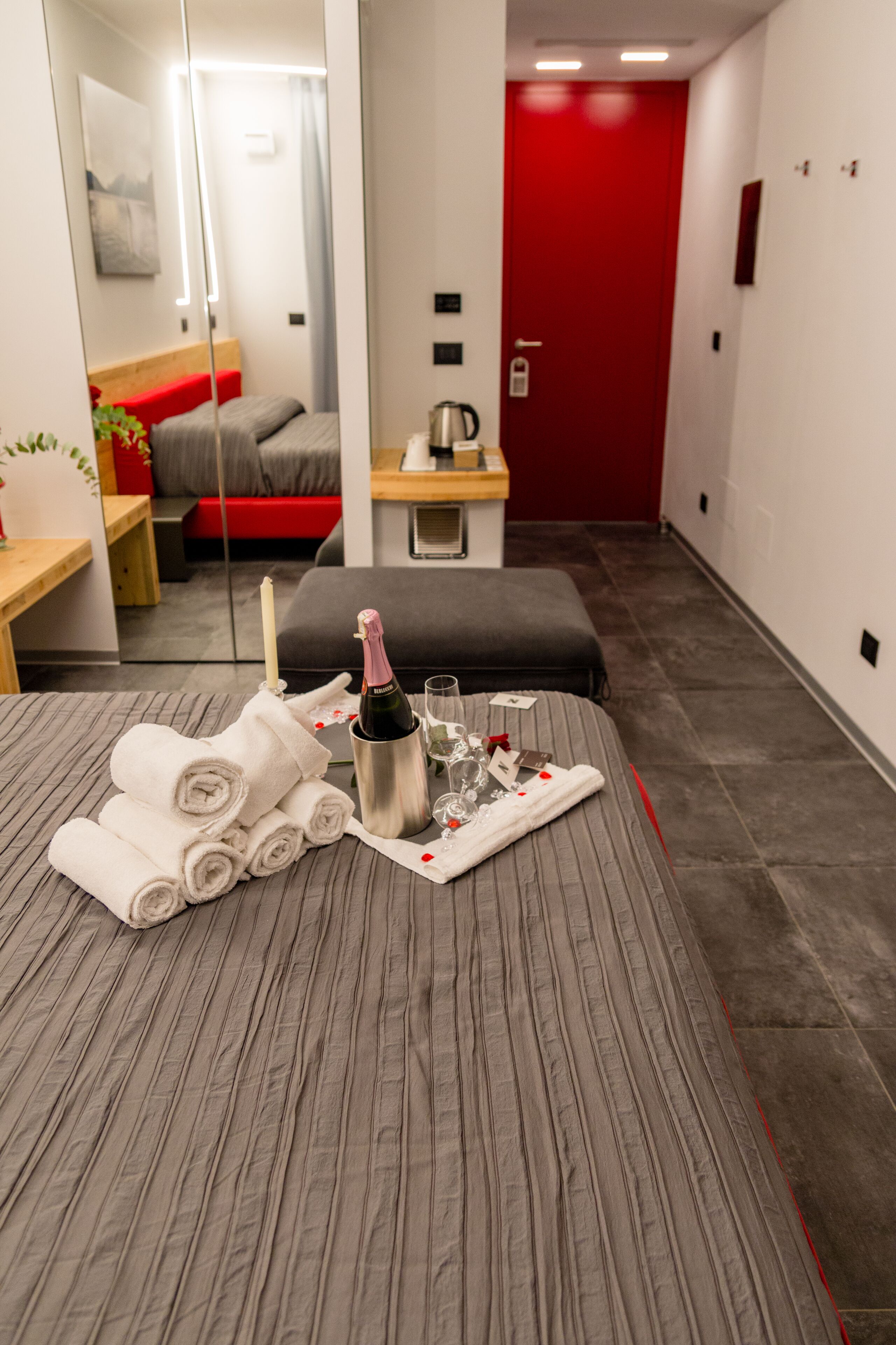 A hotel room with a bed, a bedside table with a bottle, glasses, and towels.