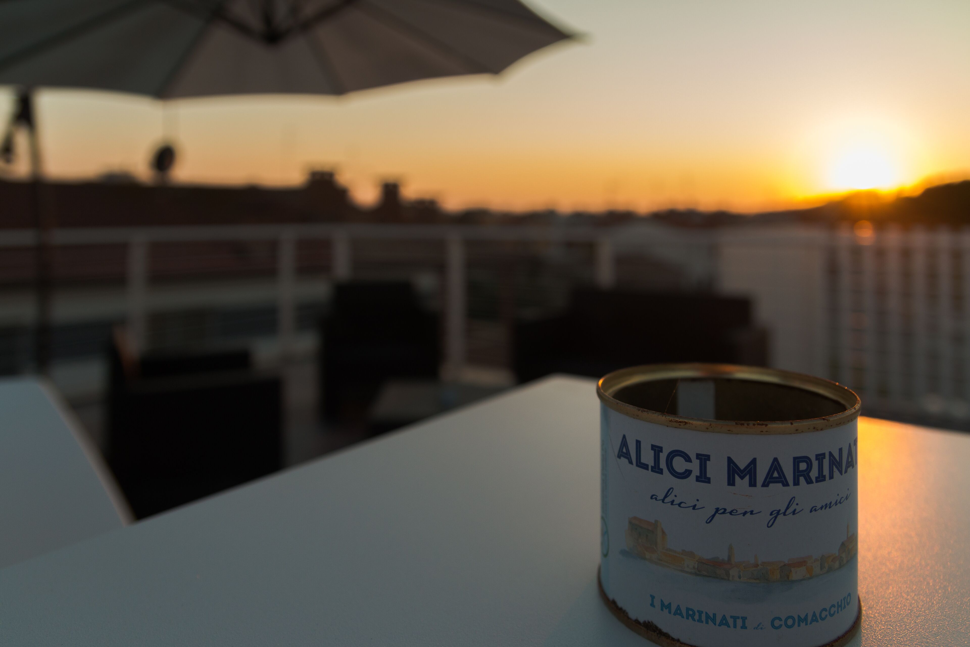 Eine Dose Alici Marina auf einem Tisch, im Hintergrund ein Sonnenuntergang.
