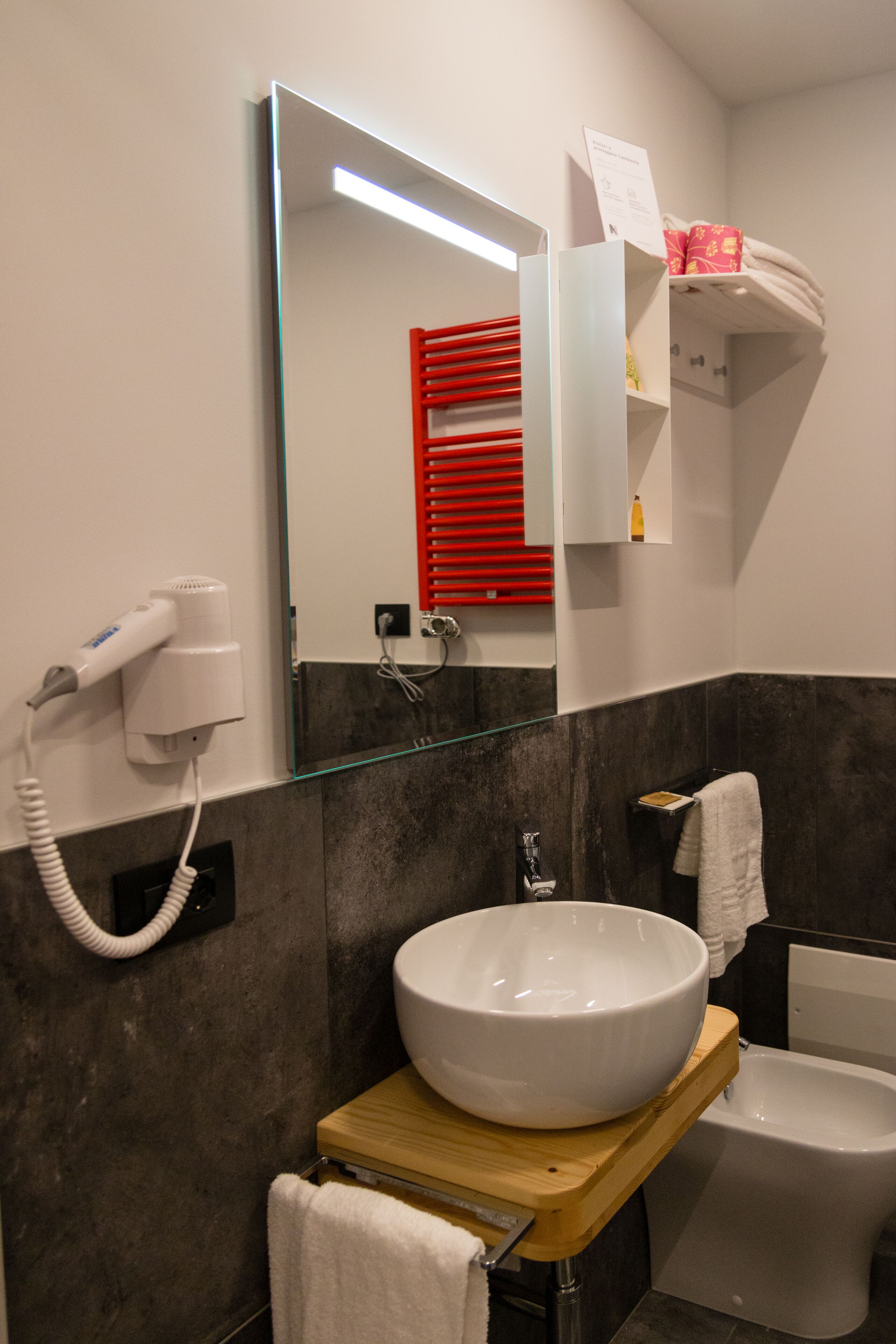 Een moderne badkamer met een grote spiegel, een witte wastafel, een toilet en een haardroger op een stopcontact.