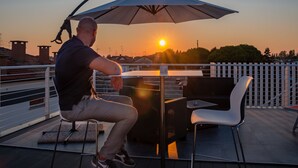 A man sitting at a table with an umbrella, overlooking a sunset. - Le Nazioni B&B (Comacchio)