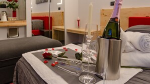 A neatly arranged hotel room with a bed, a bedside table with a bottle of champagne, a candle, and a vase with flowers. - Le Nazioni B&B (Comacchio)