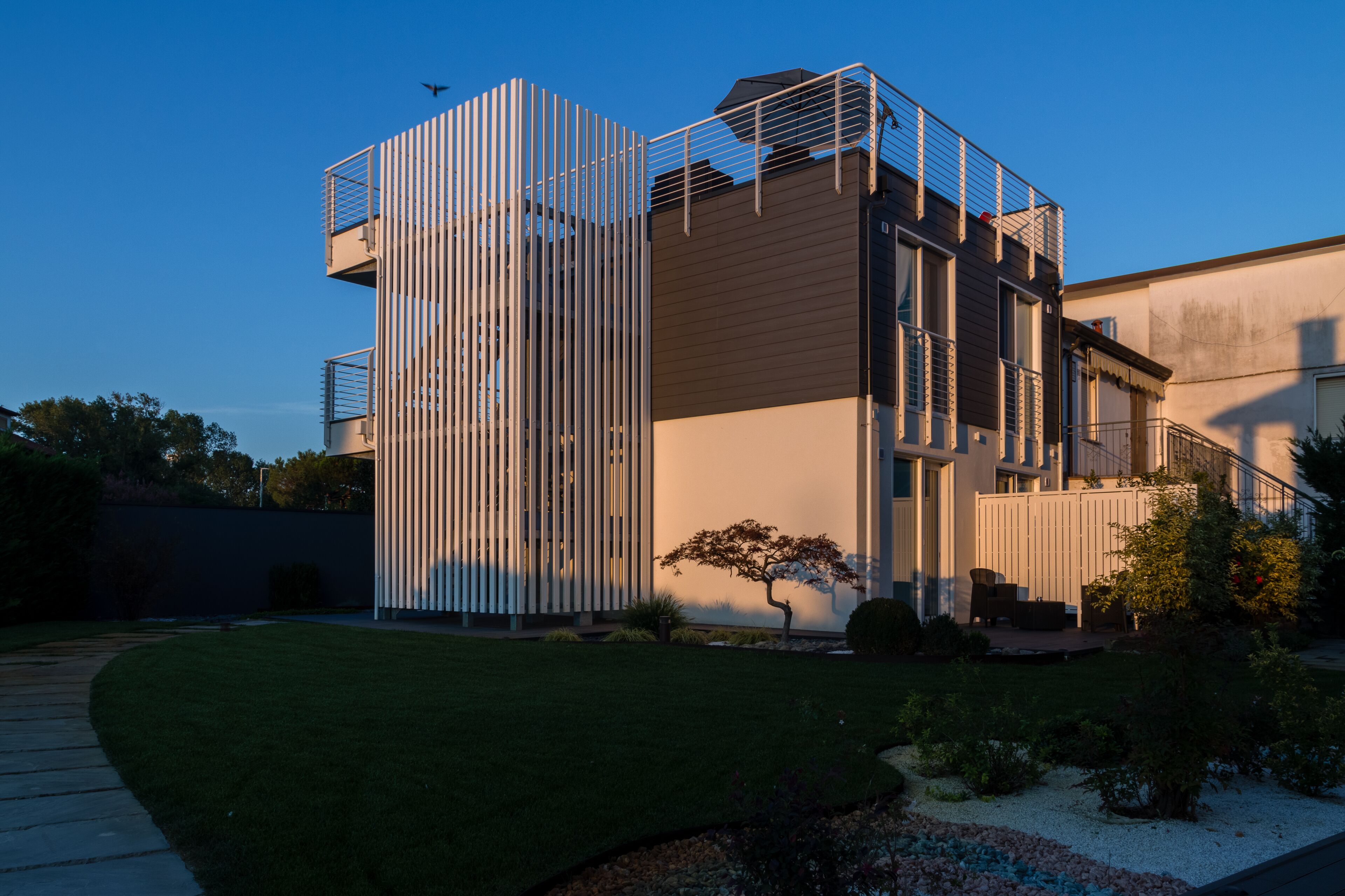 A modern building with a unique vertical design, a small garden, and a clear sky.