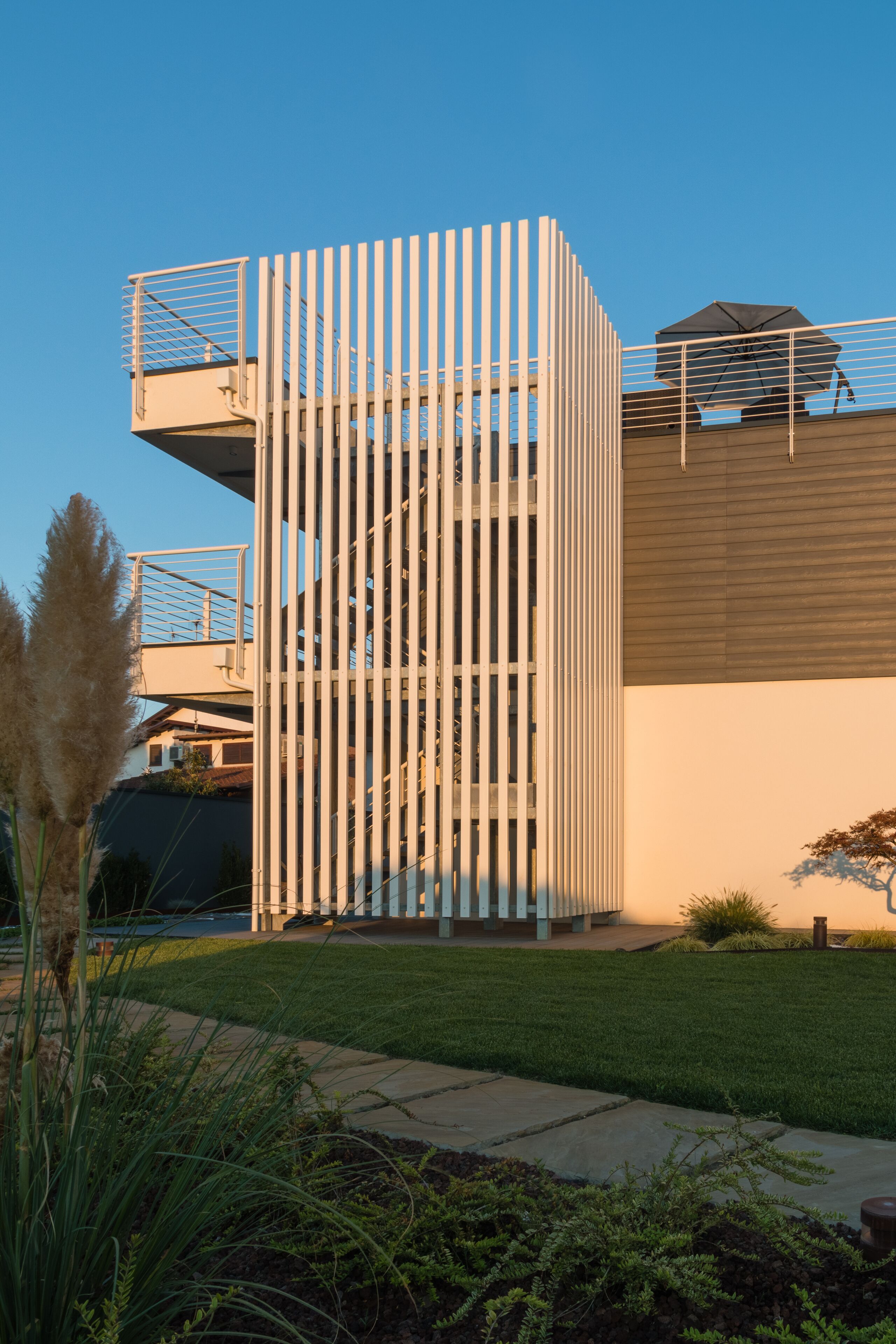 A modern building with a unique vertical structure, a rooftop terrace, and a well-maintained lawn.