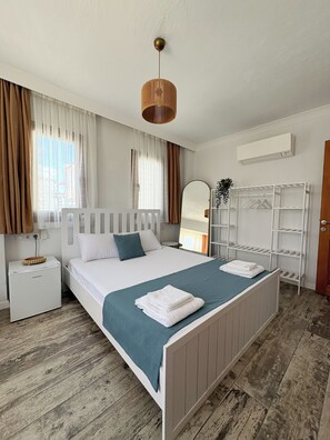 A neatly arranged bedroom with a bed, bedside tables, a wardrobe, and a hanging plant. - Sığacık Ada Pansiyon (Seferihisar)