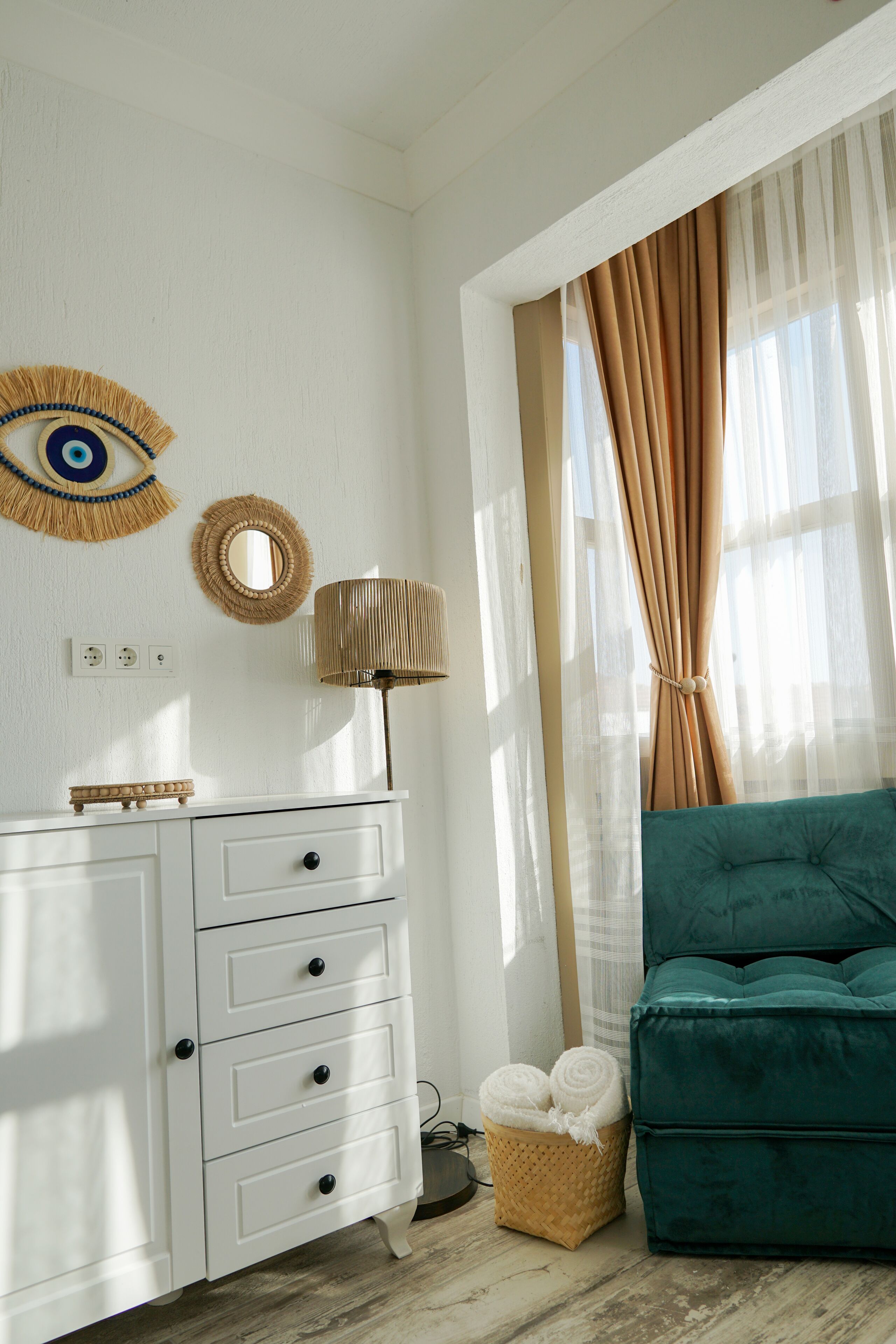 Ein Zimmer mit einem weißen Kommode, einem türkisfarbenen Sofa, einer Lampe und einem gewebten Korb mit Handtüchern.