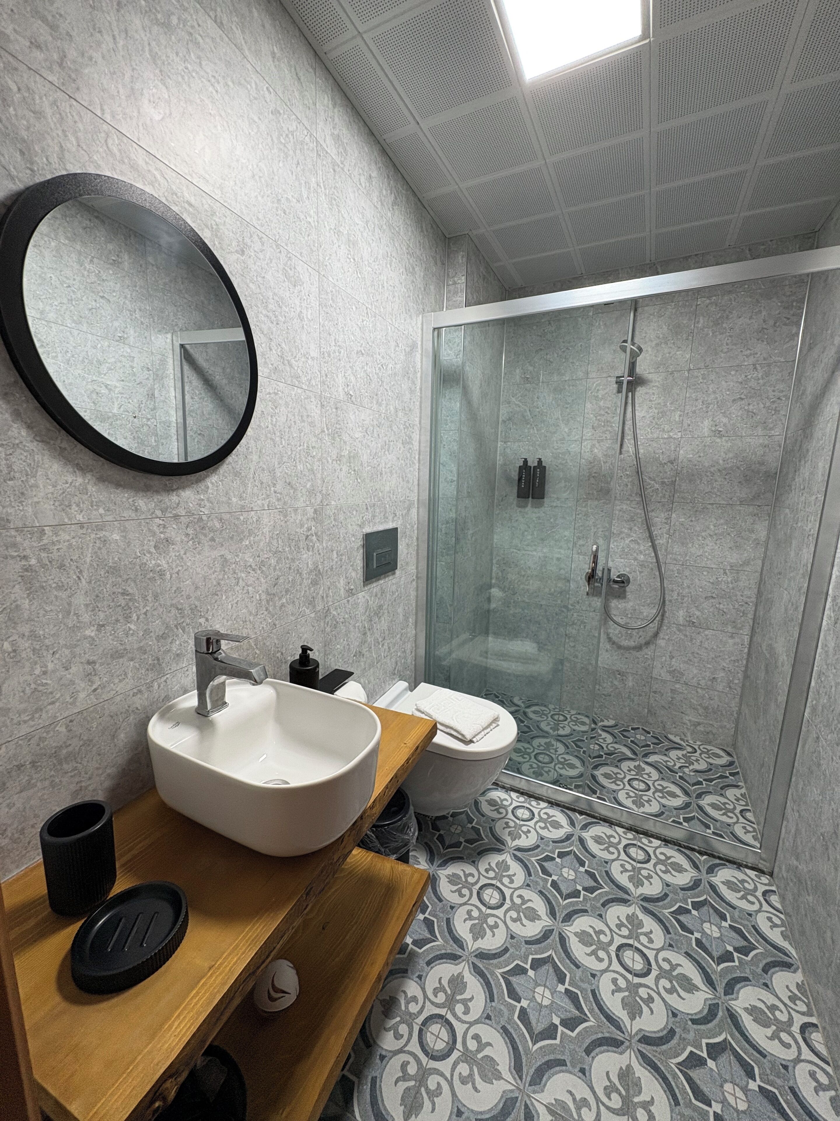 A modern bathroom with a round mirror, a sink, a toilet, and a shower area.