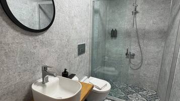 A modern bathroom with a round mirror, a sink, a toilet, and a shower area.