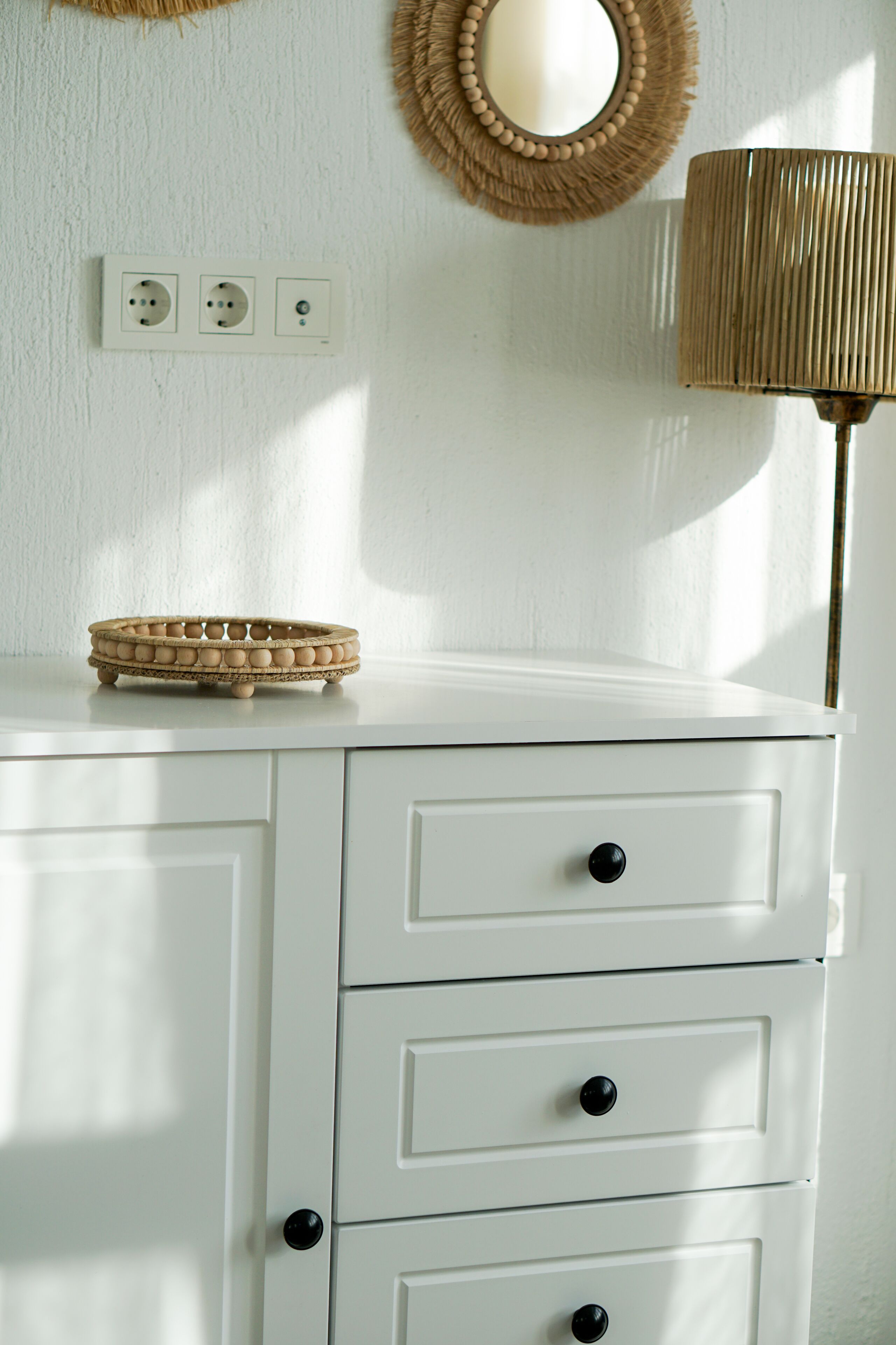 A white dresser with three drawers and a woven basket on top.