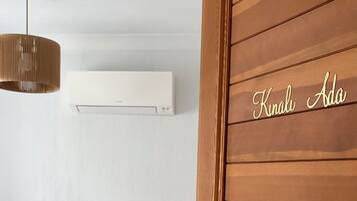 Habitación de hotel con puerta de madera, cama con ropa blanca y almohada azul, radiador blanco y lámpara colgante.