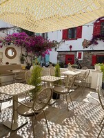Ulkoterassi, jossa on pöytiä ja tuoleja, pergola ja bougainvillea-kasveja.