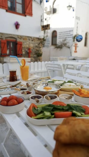Una mesa dispuesta con diversos platos, incluyendo un plato de tomates, un bol de aceitunas y un vaso de zumo de naranja.