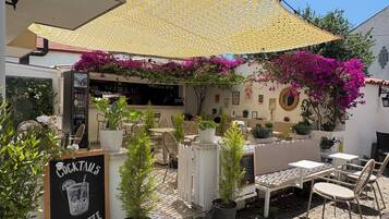 An outdoor seating area with tables and chairs, a sign for cocktails and ice coffee, and a covered section with a yellow canopy.