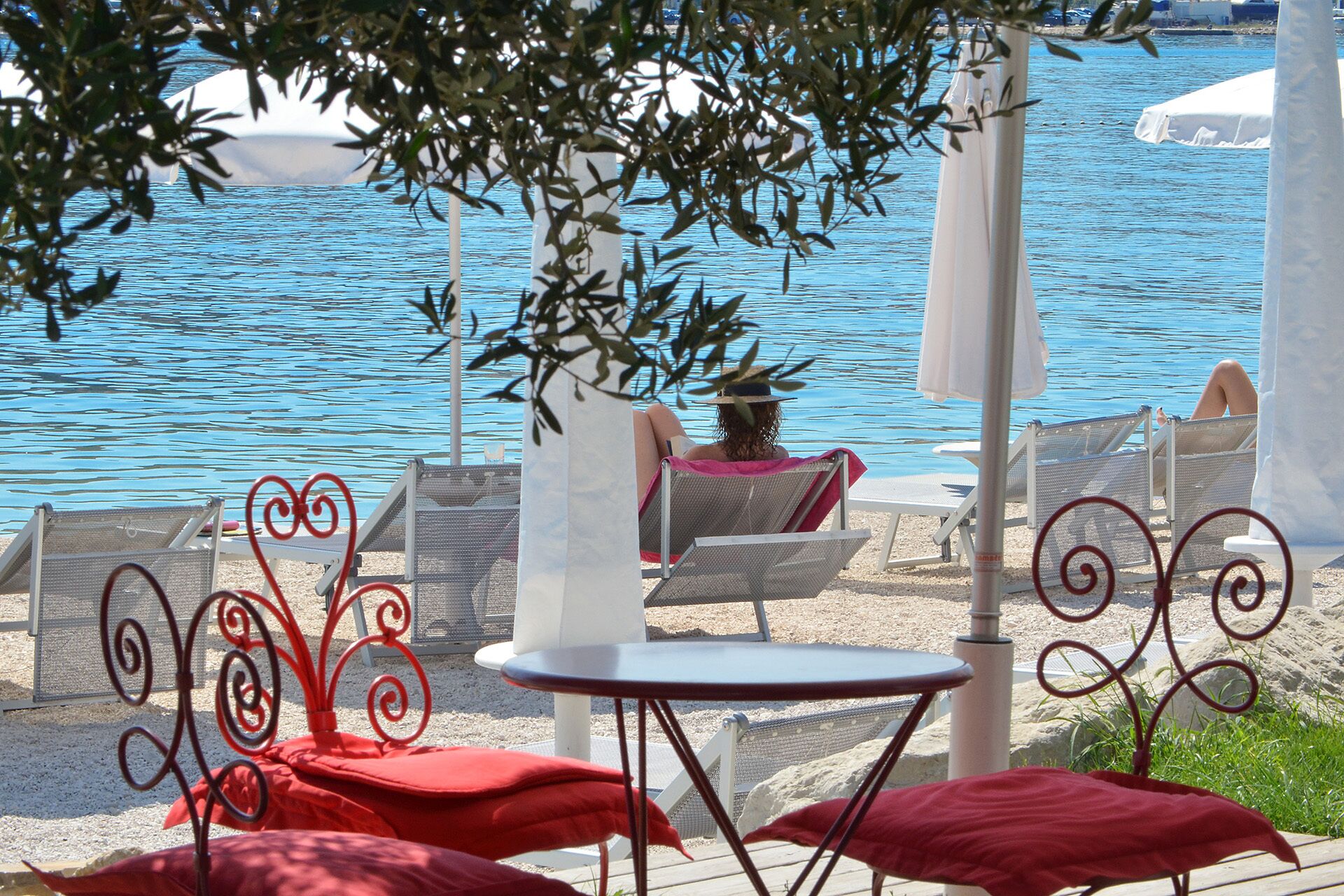 A beachside lounge area with chairs and tables, overlooking a body of water.