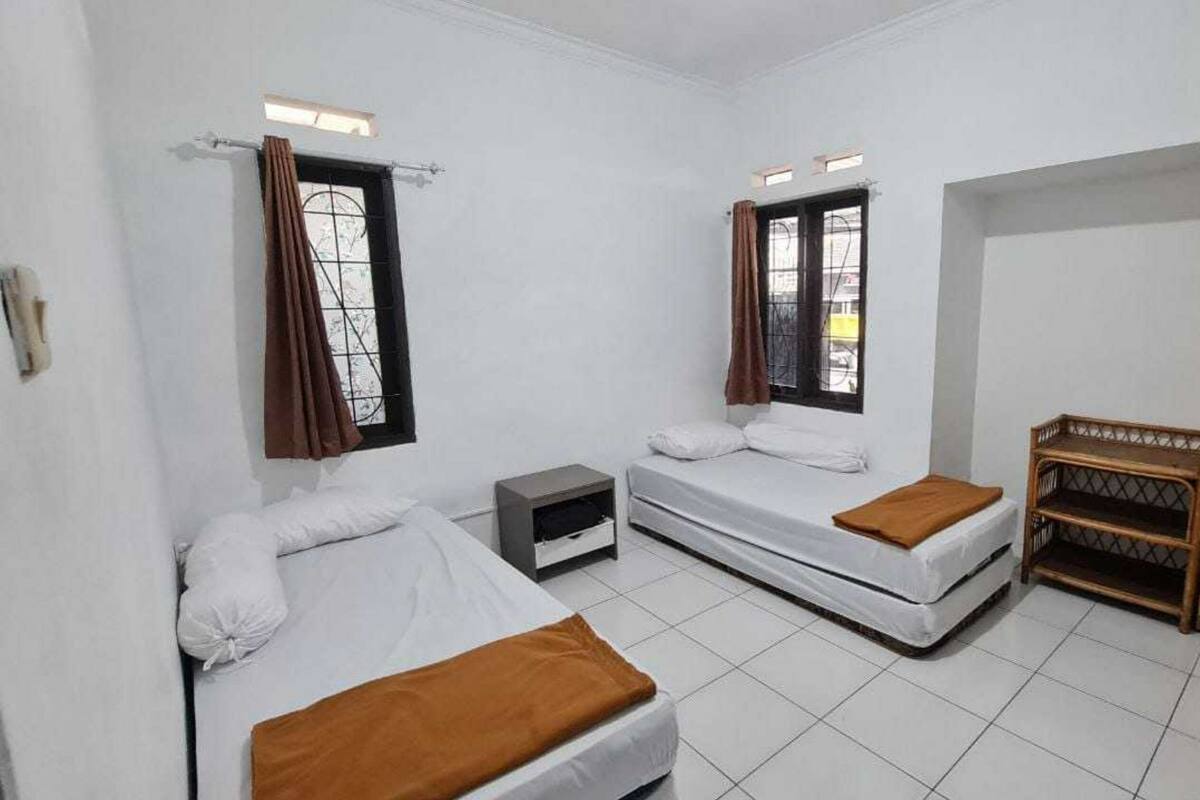 Ein Zimmer mit zwei Einzelbetten, einem Kleiderschrank, einem kleinen Tisch und einem fensterbepflanzten Fenster.