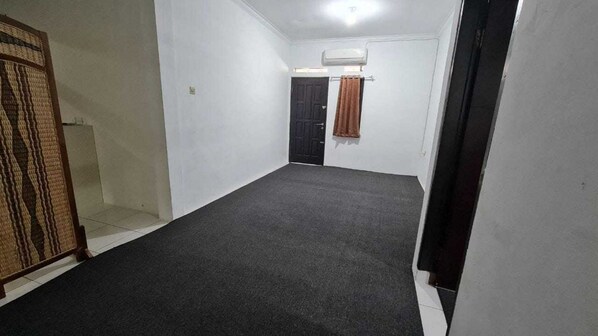 Quarto com carpete escuro, paredes brancas, porta preta e cortina marrom.
