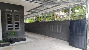 Ein überdachter Außenbereich mit Betonboden, Metallverkleidung und einer schwarzen Wand mit vertikalen Vertiefungen.