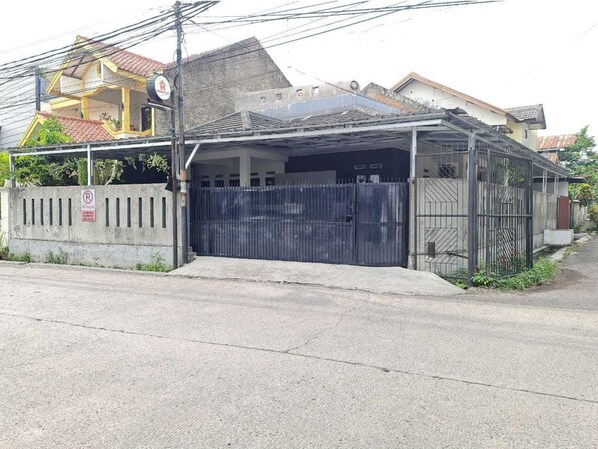 Un estacionamiento cerrado con un muro de hormigón y una puerta metálica, junto a un edificio residencial con techo de tejas.